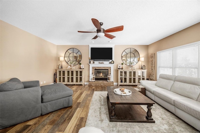 living room with ceiling fan, hardwood / wood-style floors, a textured ceiling, and a fireplace