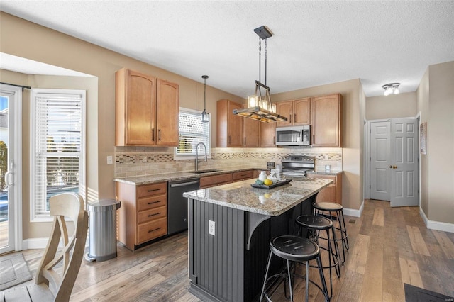 kitchen with a kitchen island, appliances with stainless steel finishes, decorative light fixtures, sink, and light hardwood / wood-style flooring