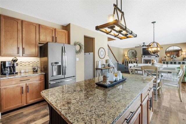 kitchen featuring stainless steel fridge, hanging light fixtures, a center island, light stone countertops, and decorative backsplash