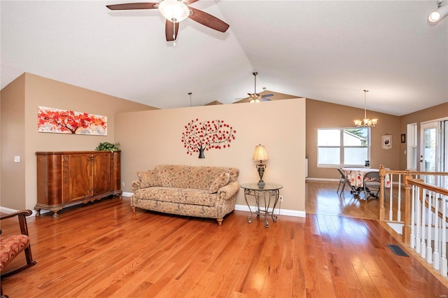 living room with ceiling fan with notable chandelier, light hardwood / wood-style flooring, and vaulted ceiling