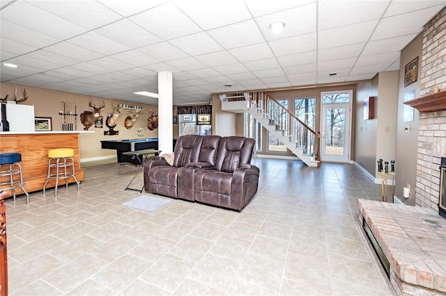 living room with light tile patterned floors, billiards, bar, a drop ceiling, and a brick fireplace