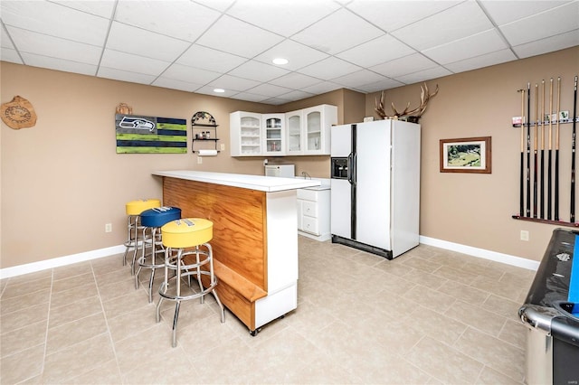 kitchen featuring a breakfast bar area, a paneled ceiling, white cabinetry, white refrigerator with ice dispenser, and kitchen peninsula