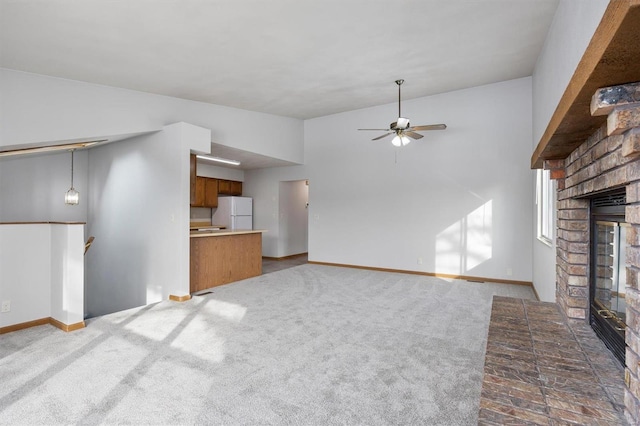 unfurnished living room with dark colored carpet, a brick fireplace, lofted ceiling, and ceiling fan