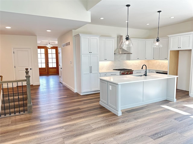 kitchen featuring wall chimney range hood, sink, white cabinets, and a center island with sink