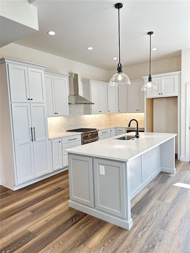 kitchen with stainless steel stove, white cabinetry, sink, wall chimney range hood, and a center island with sink