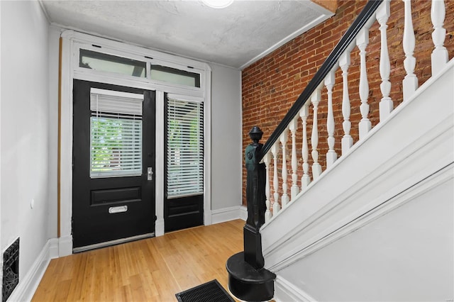 foyer entrance featuring hardwood / wood-style floors, ornamental molding, a textured ceiling, and brick wall