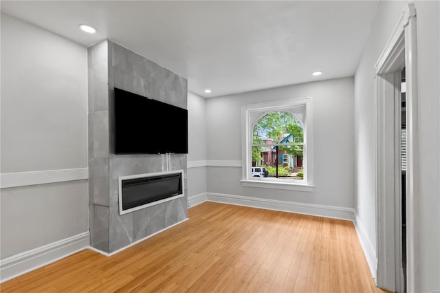 unfurnished living room with a tiled fireplace and light wood-type flooring