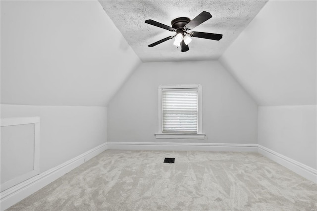 additional living space with ceiling fan, lofted ceiling, light carpet, and a textured ceiling