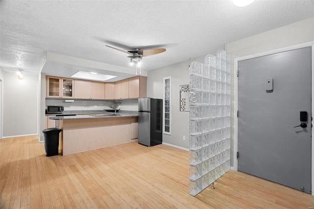 kitchen featuring appliances with stainless steel finishes, kitchen peninsula, light hardwood / wood-style floors, and light brown cabinets