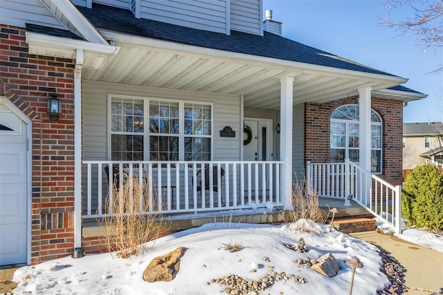 snow covered property entrance featuring a garage and covered porch