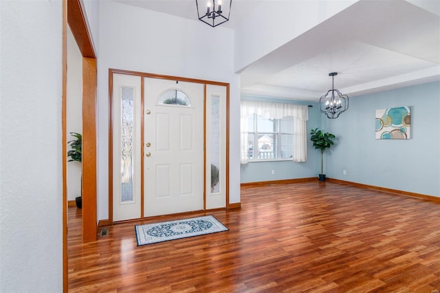 foyer entrance featuring a notable chandelier, a tray ceiling, and dark wood-type flooring