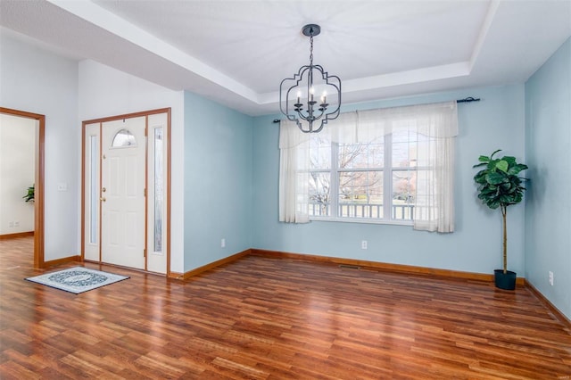 entrance foyer with dark wood-type flooring, a tray ceiling, and a chandelier