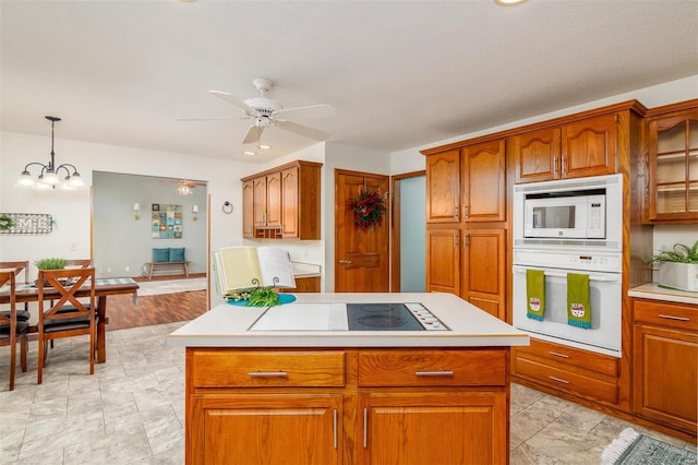 kitchen featuring ceiling fan, a center island, white appliances, and decorative light fixtures