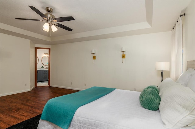 bedroom featuring hardwood / wood-style floors, ensuite bath, a raised ceiling, and ceiling fan