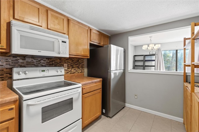 kitchen featuring a textured ceiling, a chandelier, white appliances, light countertops, and tasteful backsplash