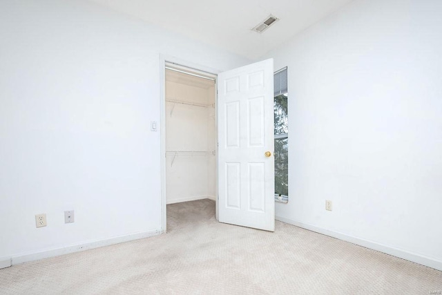 unfurnished bedroom with a walk in closet, light colored carpet, and a closet