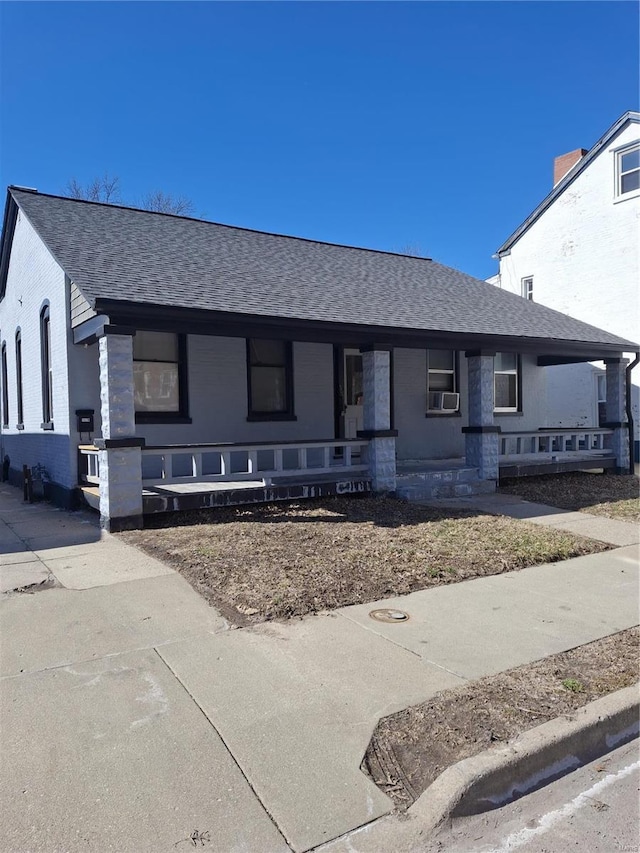 ranch-style house with covered porch, brick siding, cooling unit, and roof with shingles