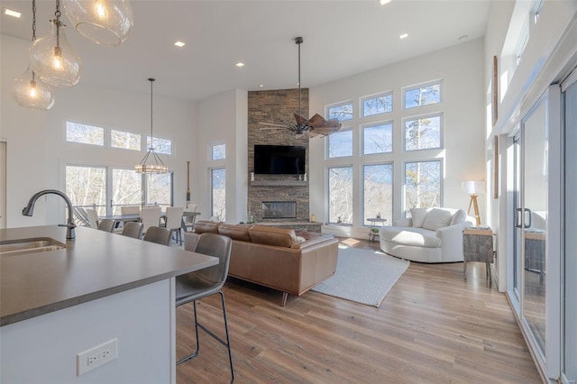 living room featuring sink, light hardwood / wood-style flooring, ceiling fan, a towering ceiling, and a fireplace