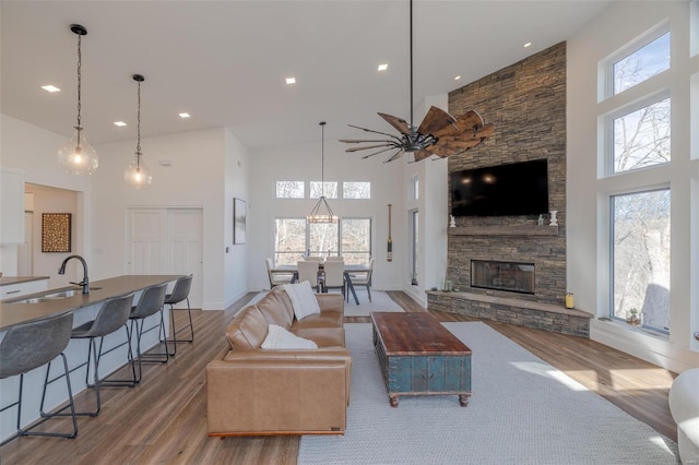 living room featuring sink, a stone fireplace, wood-type flooring, and a towering ceiling