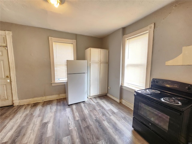 kitchen with white refrigerator, white cabinetry, black / electric stove, and plenty of natural light