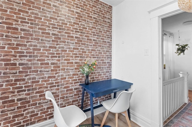 interior space featuring brick wall, wood finished floors, and baseboards