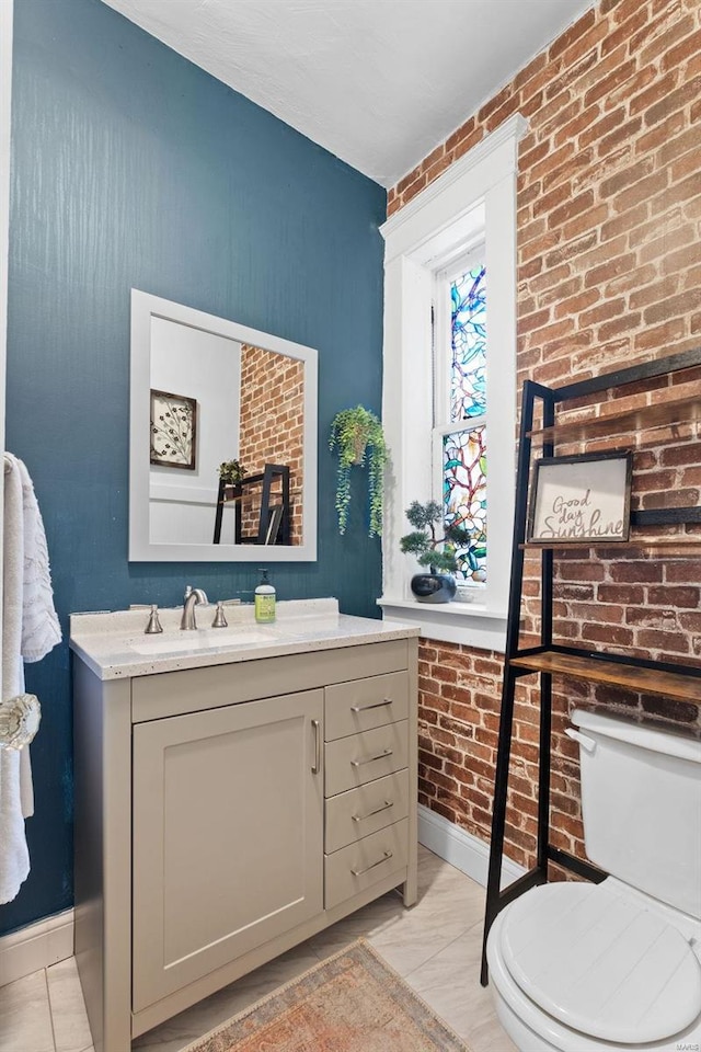 half bathroom with toilet, brick wall, baseboards, and vanity