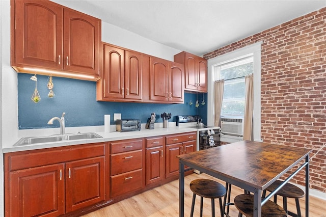 kitchen featuring light countertops, light wood-style floors, a sink, brick wall, and cooling unit