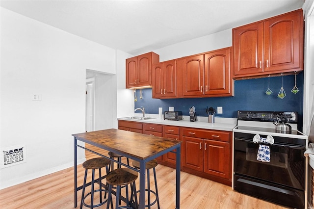 kitchen featuring light countertops, electric range, light wood-style floors, a sink, and baseboards