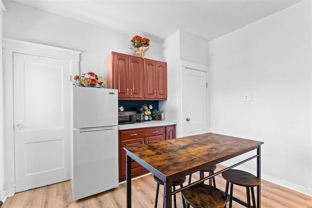 kitchen with black microwave, baseboards, light wood-style floors, light countertops, and freestanding refrigerator