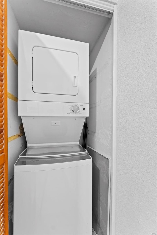 clothes washing area with laundry area, a textured wall, and stacked washing maching and dryer