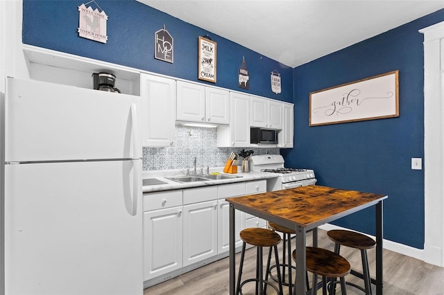 kitchen with white appliances, light countertops, light wood-type flooring, white cabinetry, and a sink