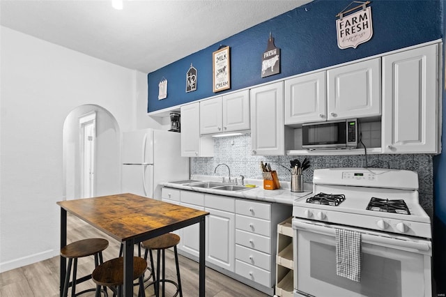 kitchen with light countertops, decorative backsplash, white cabinetry, a sink, and white appliances