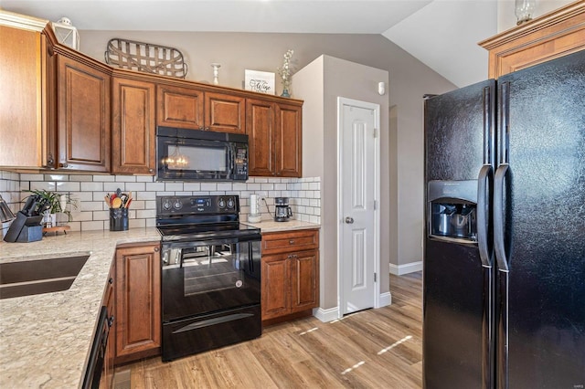 kitchen featuring sink, black appliances, decorative backsplash, vaulted ceiling, and light wood-type flooring