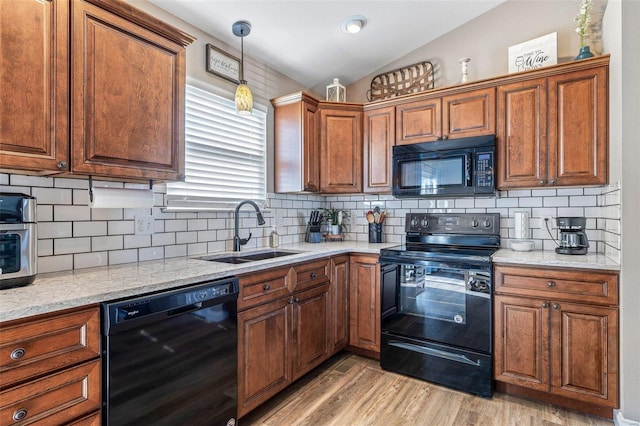 kitchen with lofted ceiling, sink, light stone counters, light wood-type flooring, and black appliances