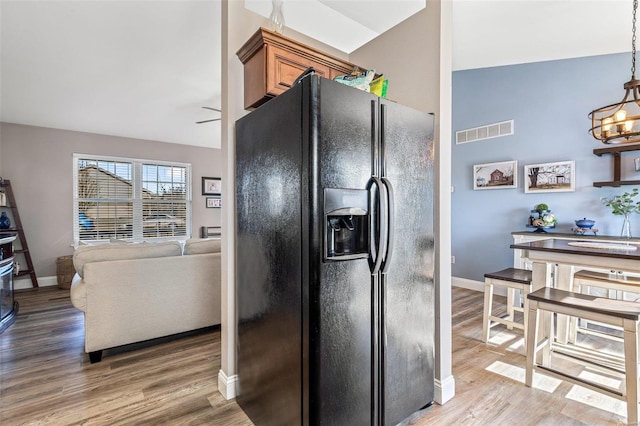 kitchen featuring pendant lighting, hardwood / wood-style flooring, an inviting chandelier, and black fridge