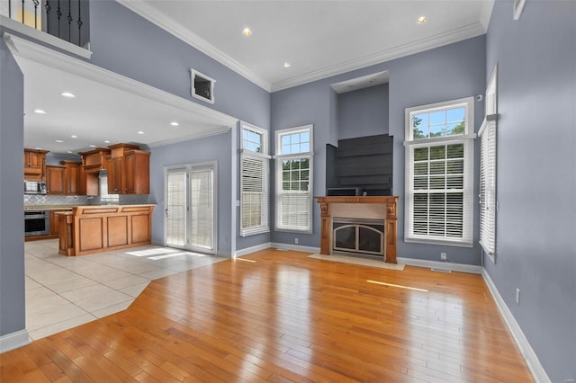 unfurnished living room featuring a high ceiling, crown molding, plenty of natural light, and light wood-type flooring