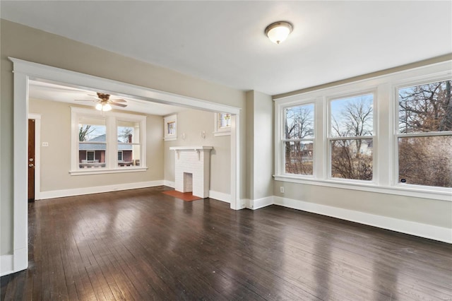 unfurnished living room with dark wood-style flooring, a fireplace, baseboards, and ceiling fan