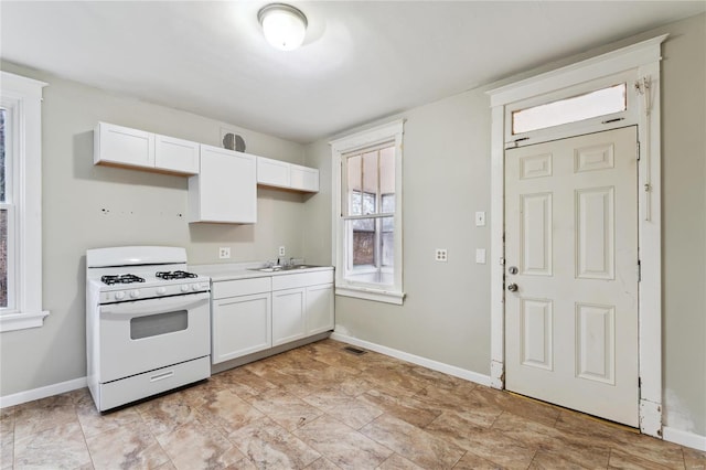 kitchen featuring white gas range, baseboards, and white cabinets