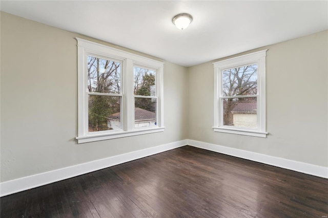 spare room featuring dark wood-style flooring, plenty of natural light, and baseboards