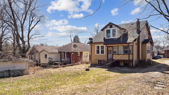 view of front facade featuring a chimney, stucco siding, a shingled roof, entry steps, and a front lawn