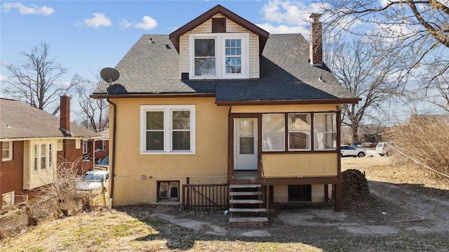 rear view of property featuring entry steps, stucco siding, a chimney, and roof with shingles