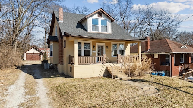 bungalow featuring a shingled roof, a chimney, an outdoor structure, a porch, and stucco siding