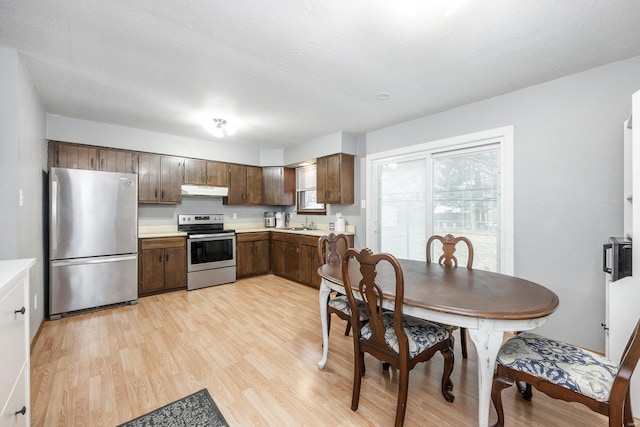 kitchen with sink, a textured ceiling, dark brown cabinets, light wood-type flooring, and appliances with stainless steel finishes