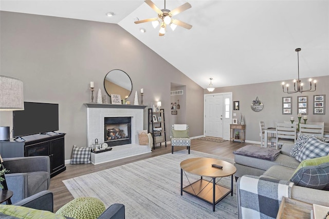 living room featuring hardwood / wood-style floors, ceiling fan with notable chandelier, a fireplace, and high vaulted ceiling