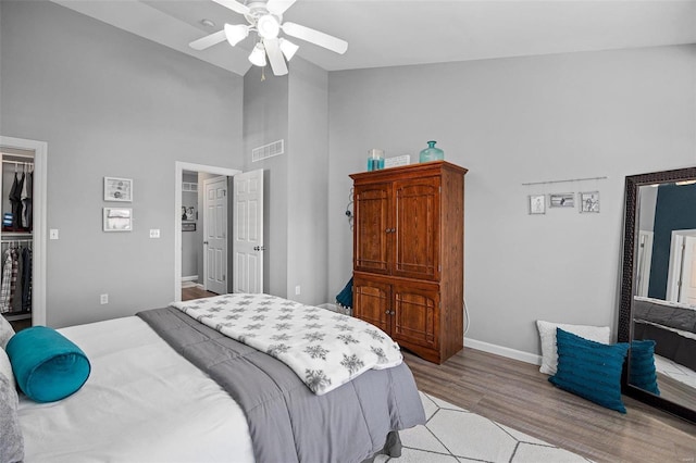 bedroom with a spacious closet, a closet, ceiling fan, light hardwood / wood-style floors, and a high ceiling