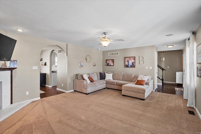 living room with a textured ceiling, a fireplace, ceiling fan, and carpet