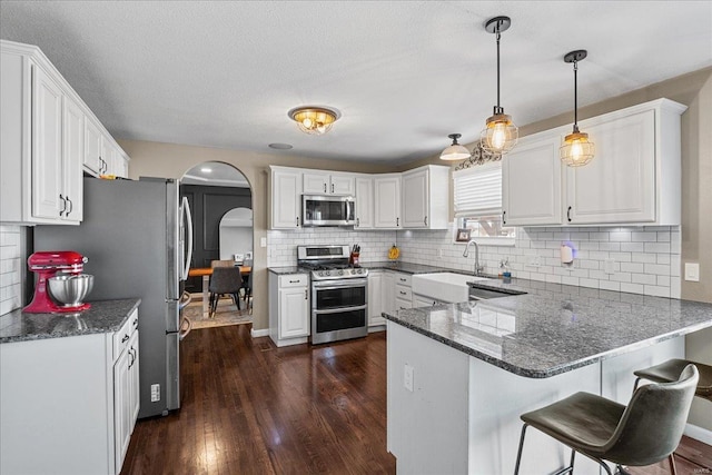 kitchen with pendant lighting, sink, stainless steel appliances, white cabinets, and kitchen peninsula