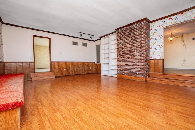 unfurnished living room featuring hardwood / wood-style flooring, ornamental molding, rail lighting, and wood walls