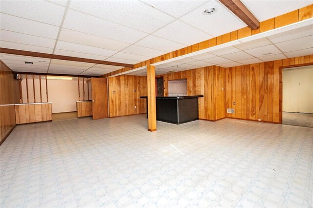 basement with a drop ceiling and wooden walls