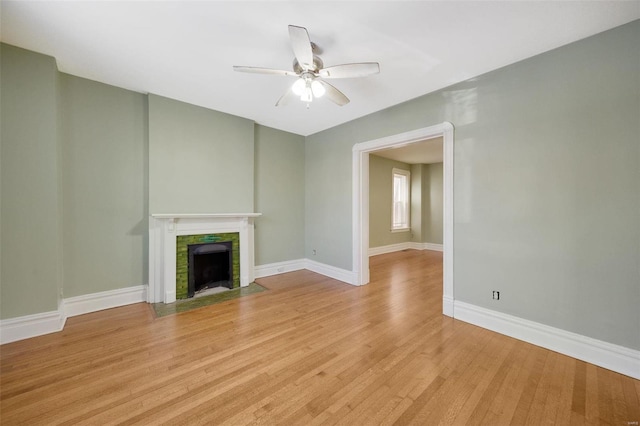 unfurnished living room with ceiling fan, a tiled fireplace, and light hardwood / wood-style floors